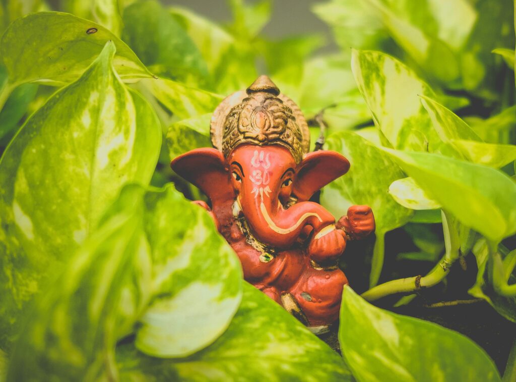 About us A vibrant Ganesha idol surrounded by lush green leaves, representing spirituality and nature.